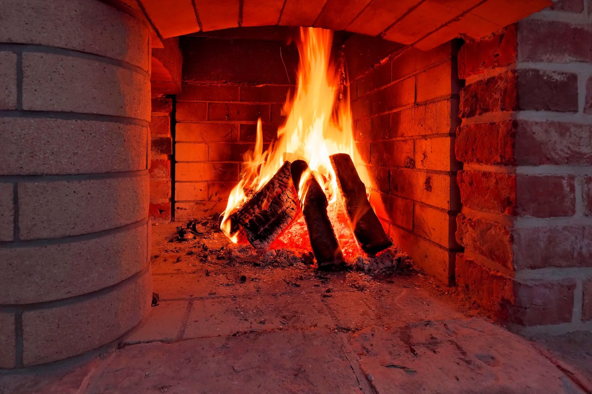 Lit fireplace with glowing logs and flames inside a brick-lined hearth. Lit fireplace with glowing logs and flames inside a brick-lined hearth.