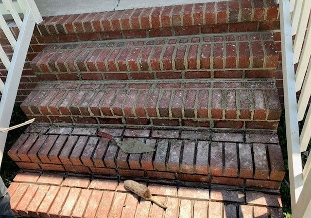 Brick steps leading up to a building, with a white railing on the sides. A trowel and other debris sit on the bottom step.