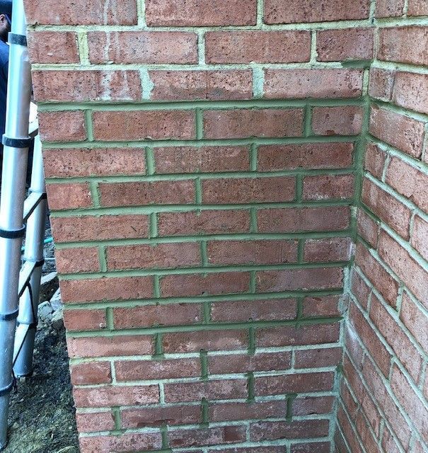 Red brick corner of a building with green mortar. A ladder leans against the left side.