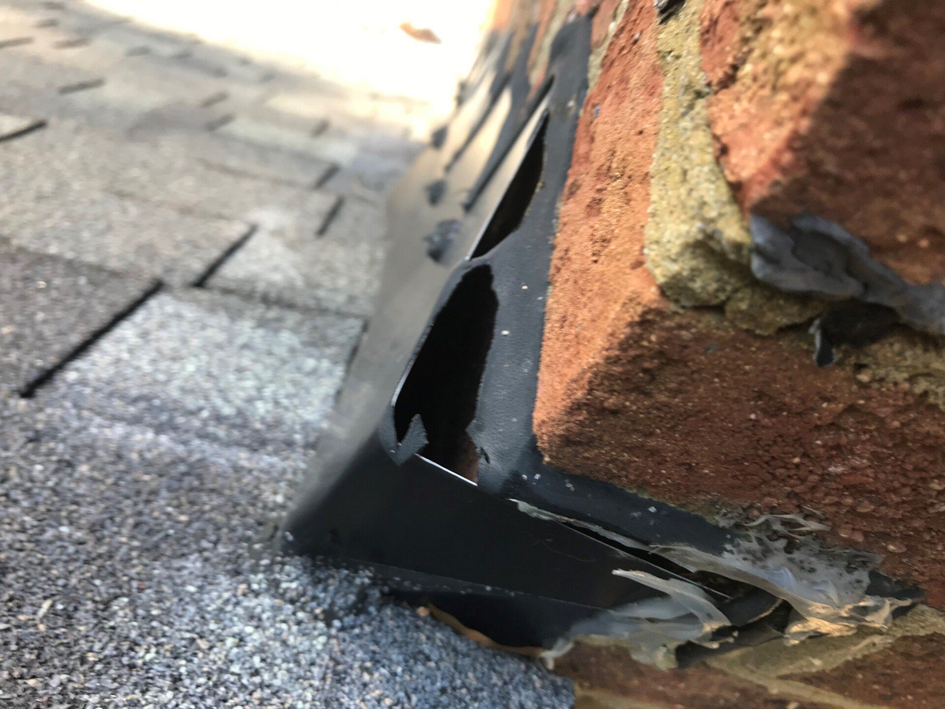 Close-up of roof flashing against a brick chimney, showing a black, metal piece with a tear and gaps