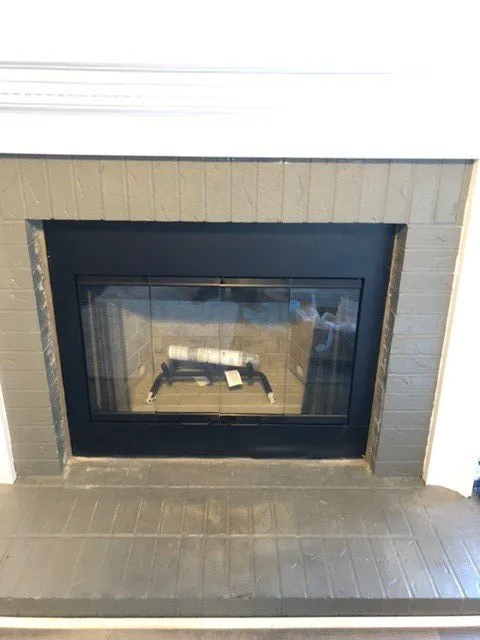 A fireplace with a black frame and gray tile surround, viewed straight on. The mantel is white.