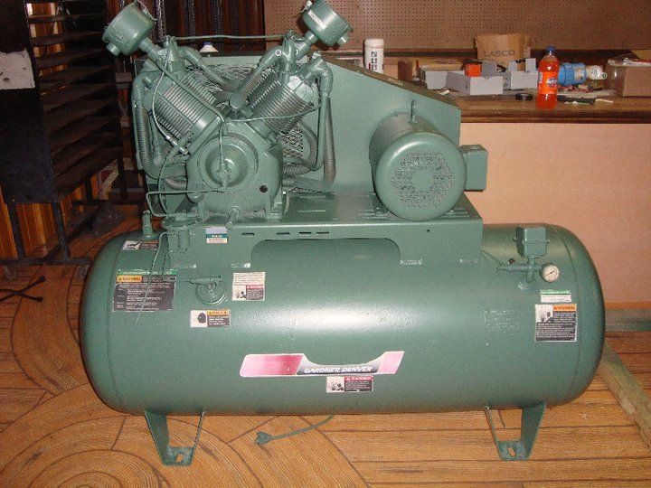 A green air compressor is sitting on a wooden floor