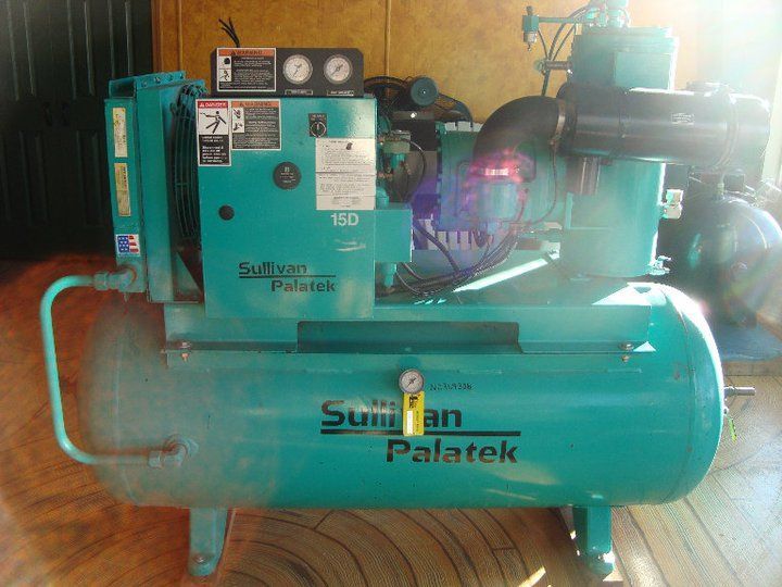 A blue air compressor is sitting on a wooden floor