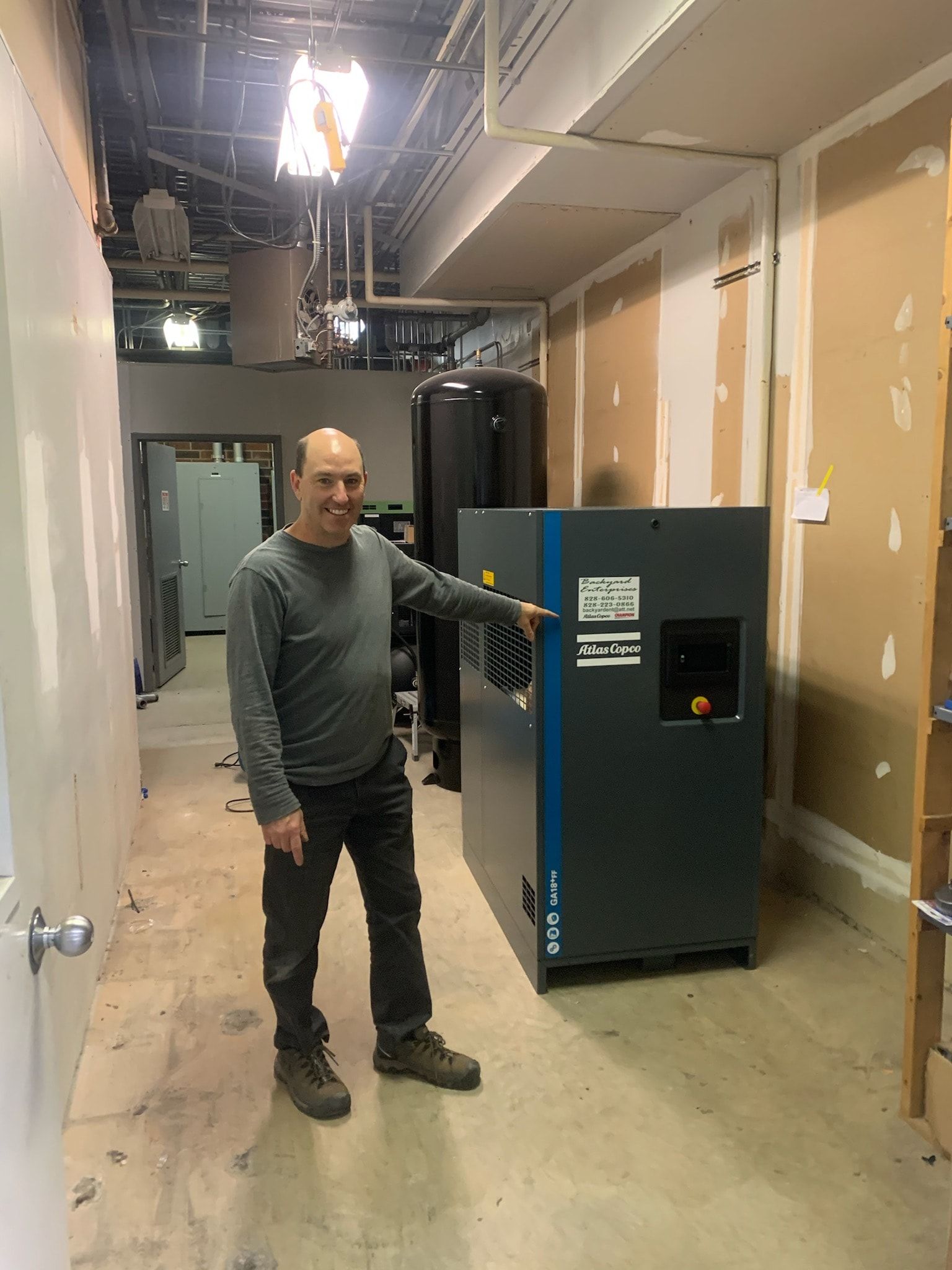 A man is standing in a hallway pointing at a machine.