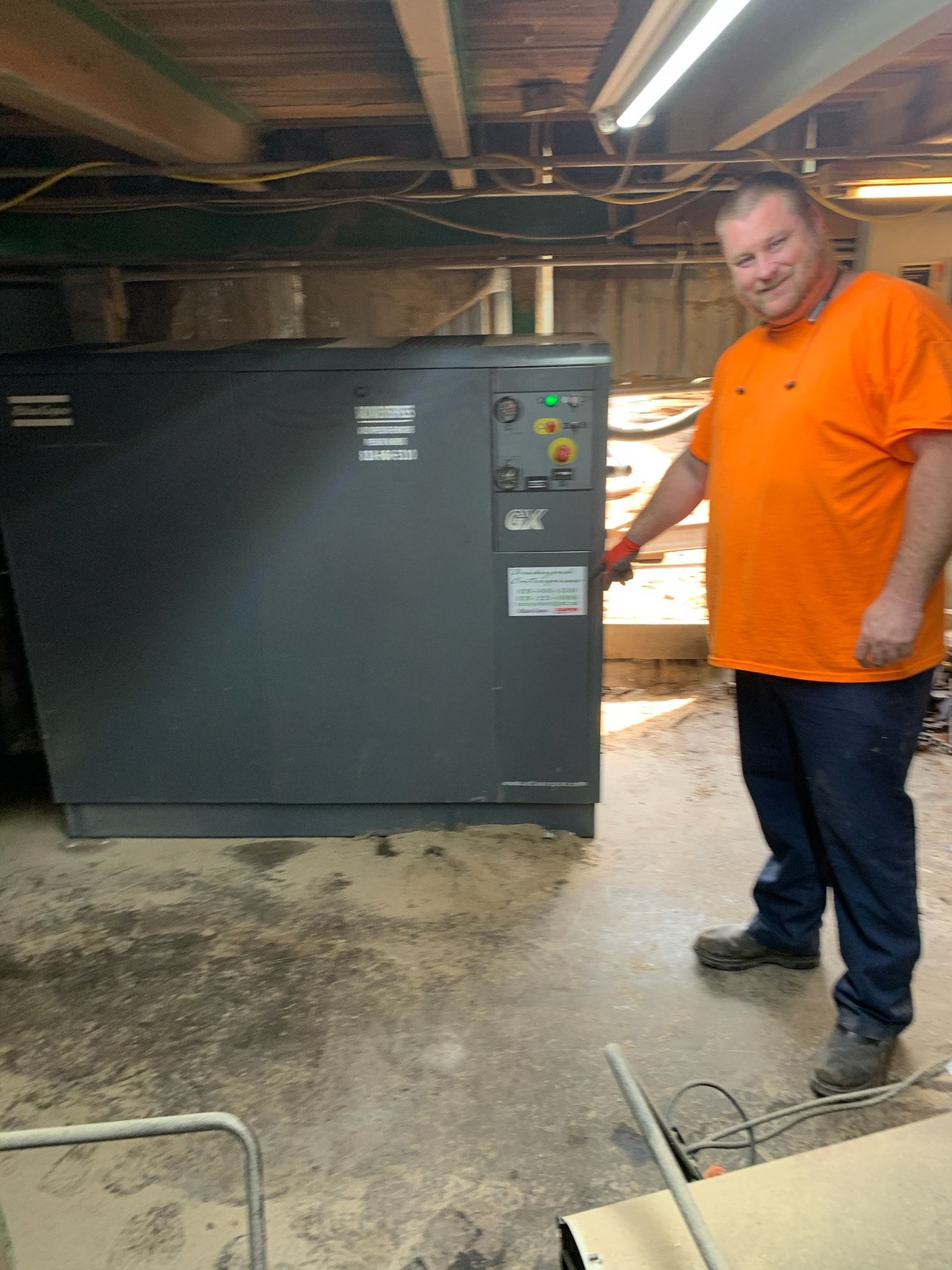 A man in an orange shirt is standing in front of a machine.