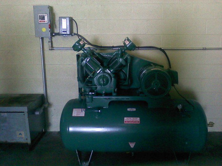 A green air compressor is sitting in a room next to a brick wall