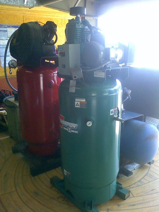 Two air compressors are sitting next to each other on a wooden floor.