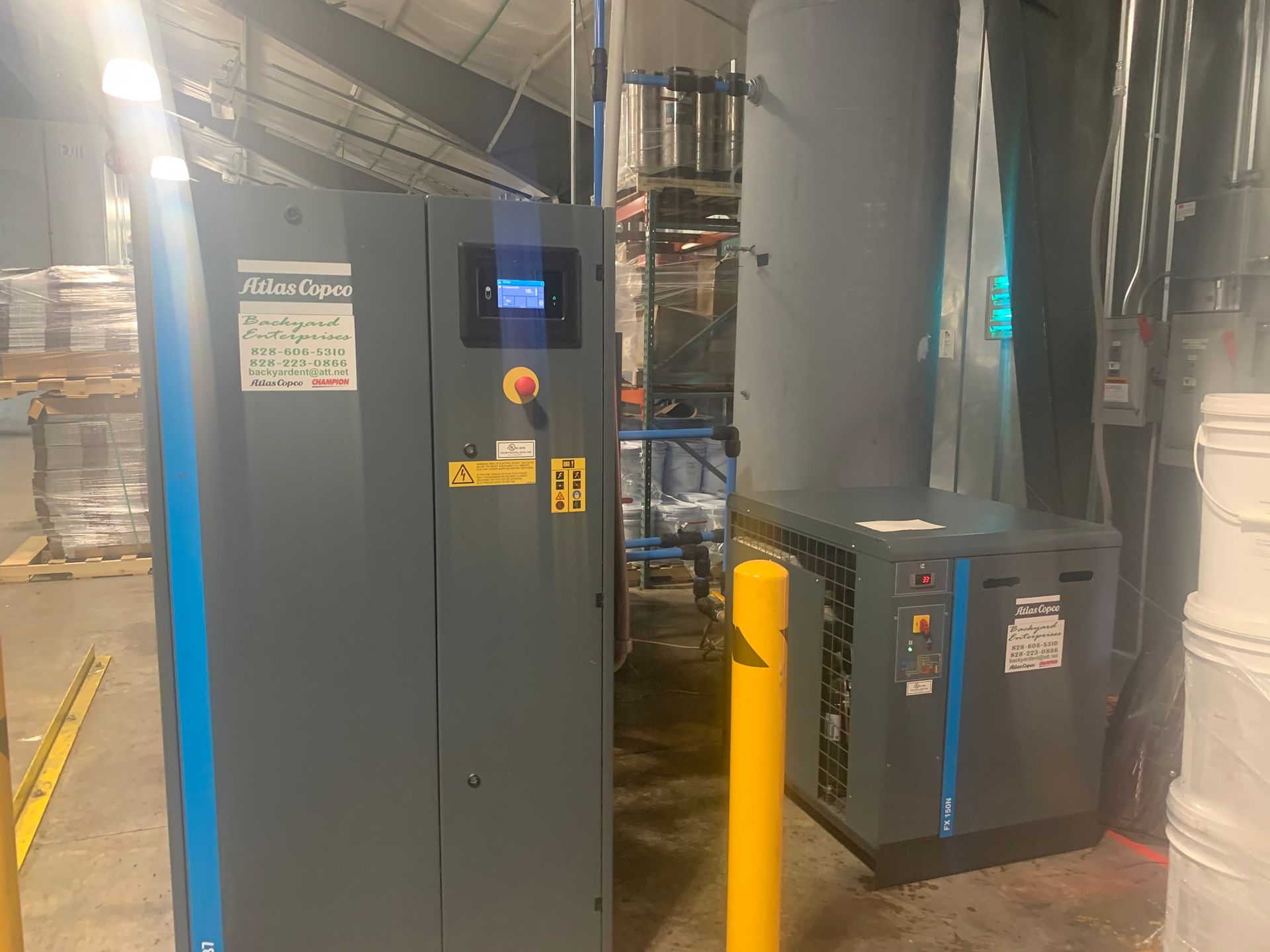 A large air compressor is sitting in a warehouse next to a large tank.