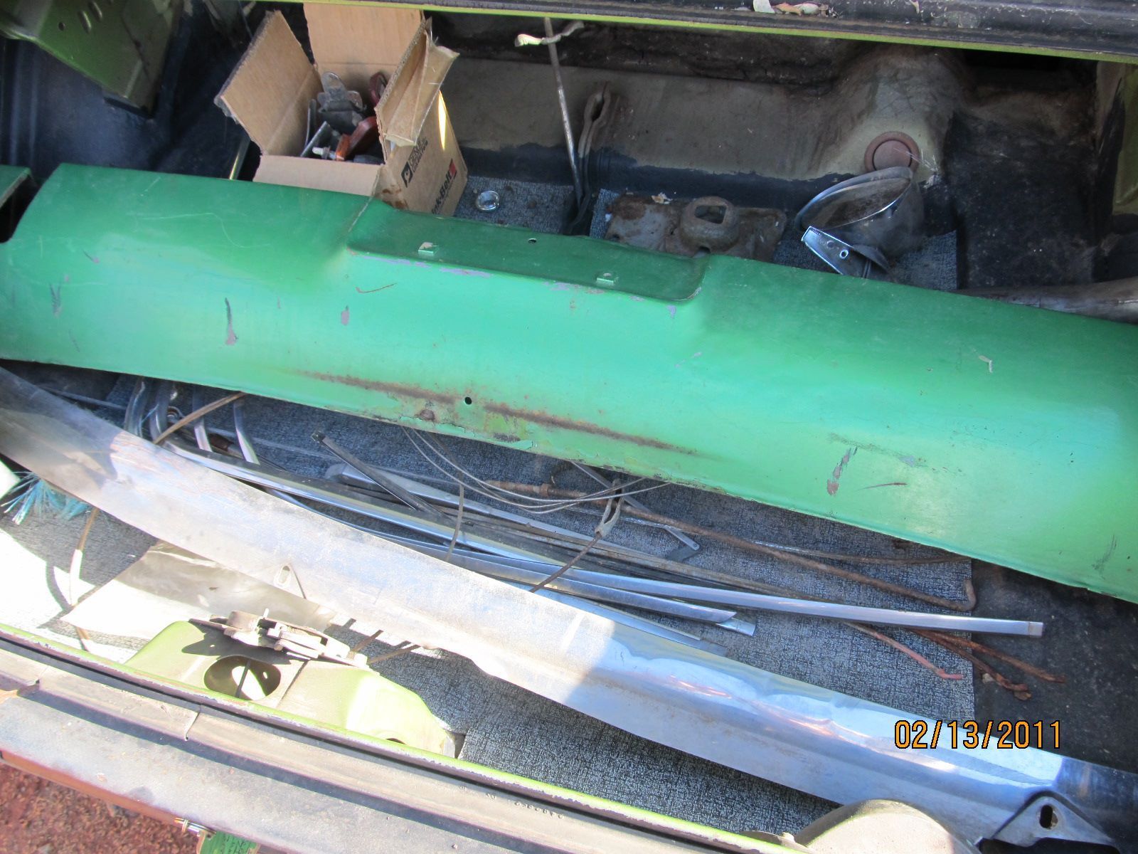 A green bumper is sitting in the trunk of a car.