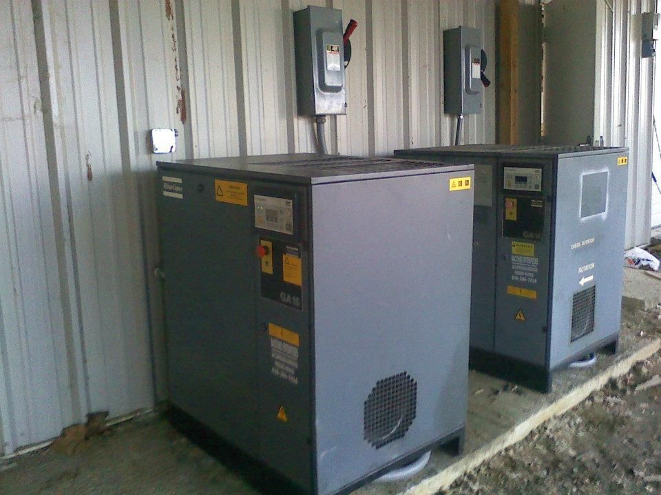 Two air compressors are sitting outside of a building