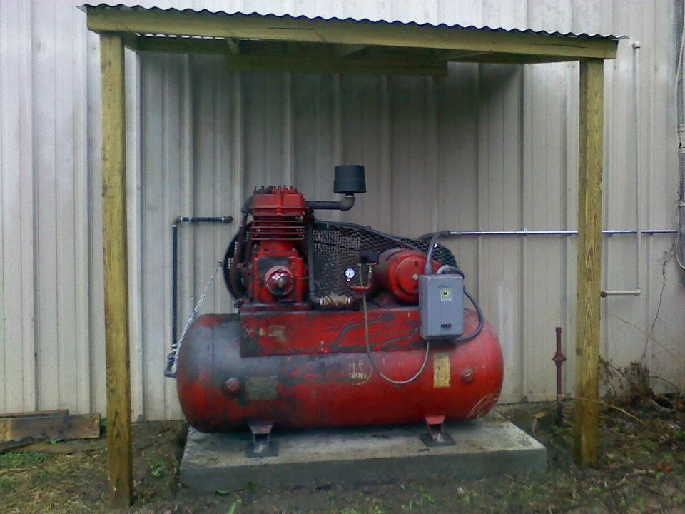 A red air compressor is sitting under a wooden structure.