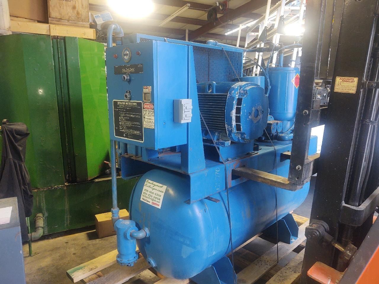 A blue air compressor is sitting in a warehouse next to a forklift.
