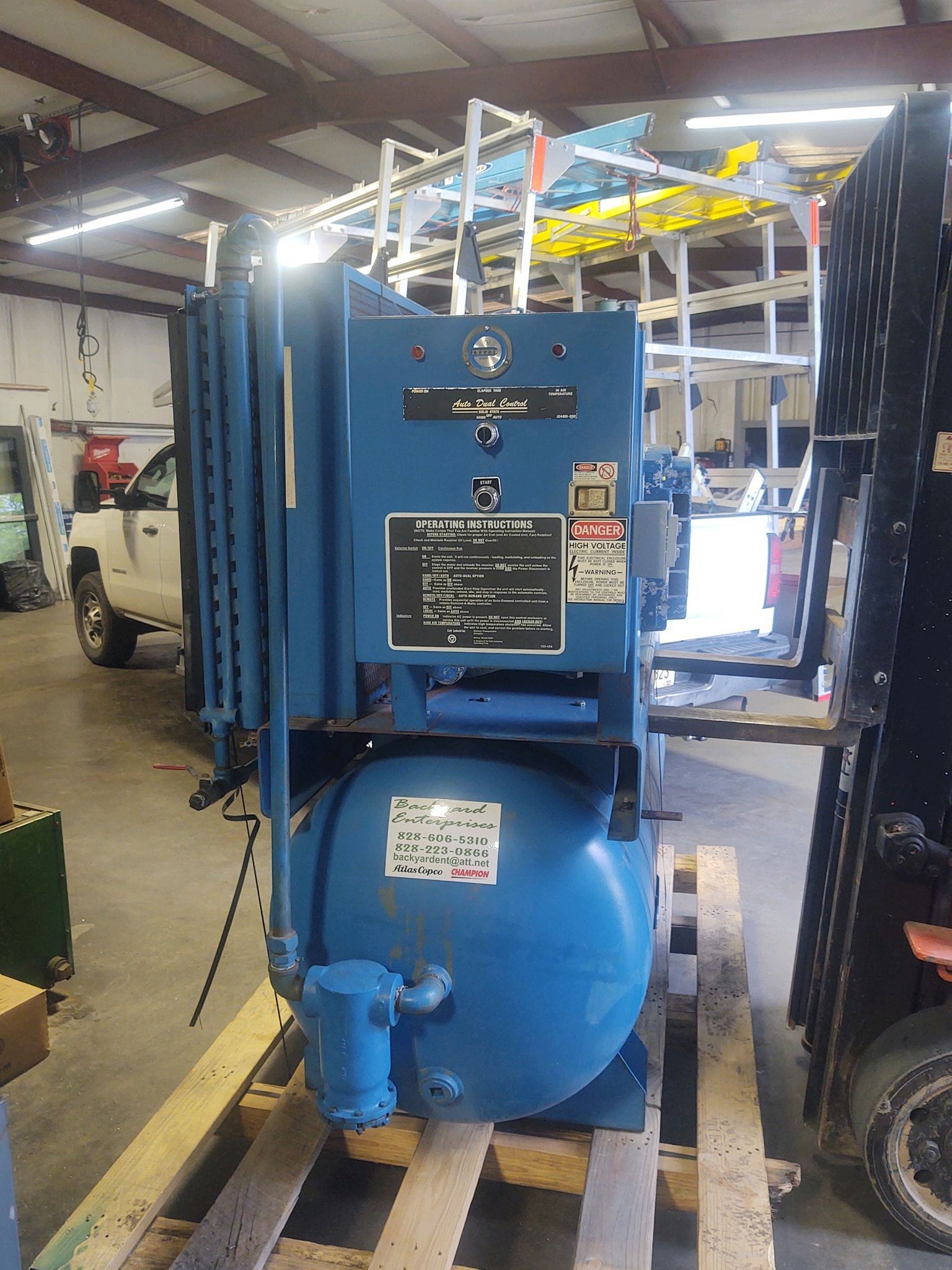 A blue air compressor is sitting on a wooden pallet in a garage.