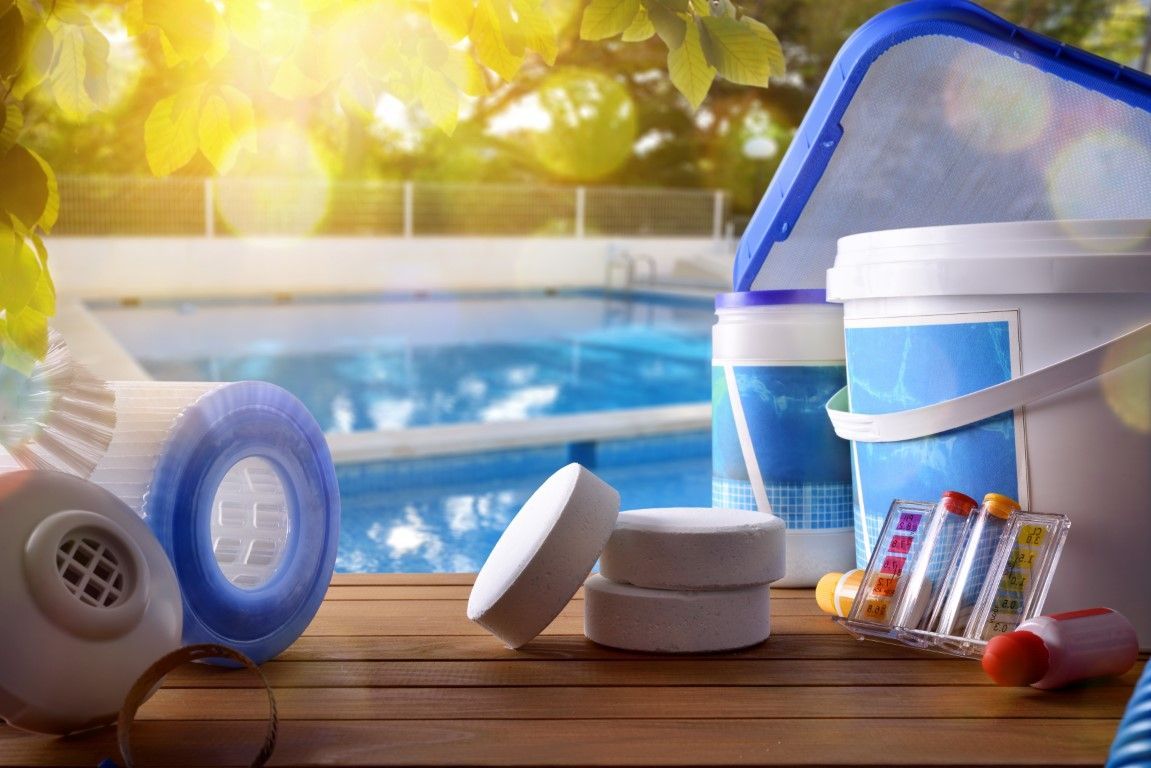 Poolside assortment of chlorine tablets, test strips, skimmer, and cleaning supplies by a swimming pool