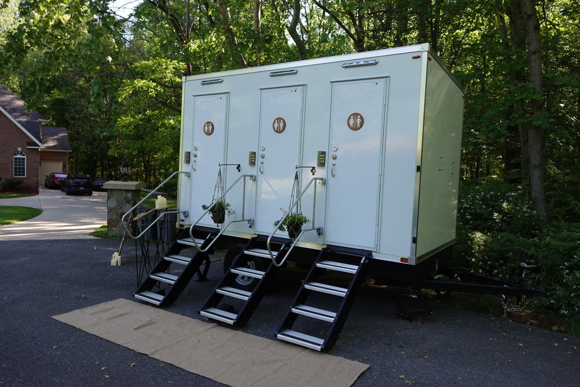 A white trailer with three toilets and stairs is parked in a driveway.