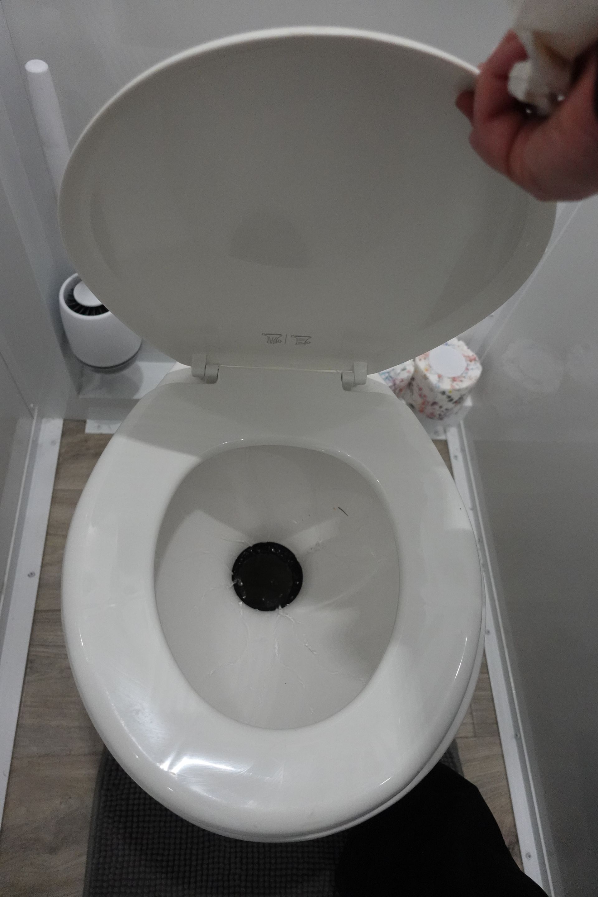 A person is holding the lid of a toilet in a bathroom.