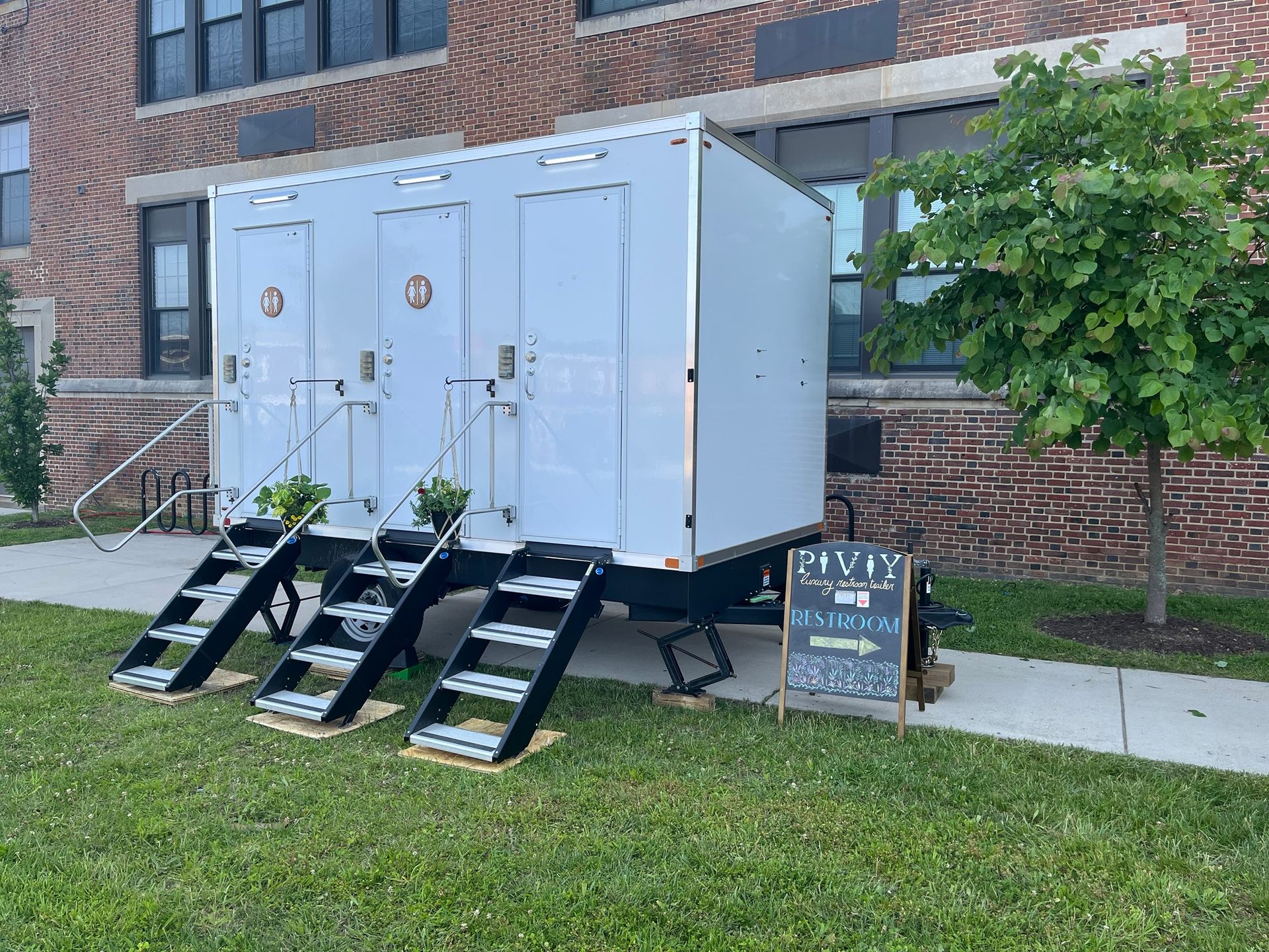 A white trailer with stairs attached to it is parked in front of a brick building.