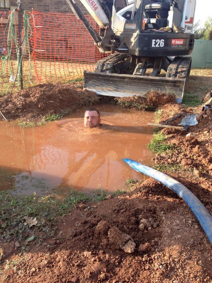 A man is swimming in a puddle of mud next to a bulldozer.
