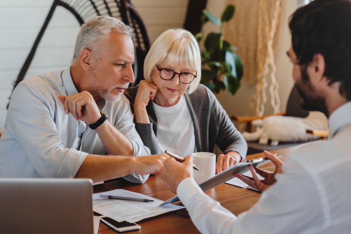 Older couple reviews document with advisor at a table, using a tablet.