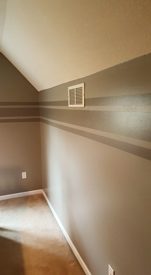 A corner of a room with beige walls featuring two horizontal gray accent stripes and a white air vent.