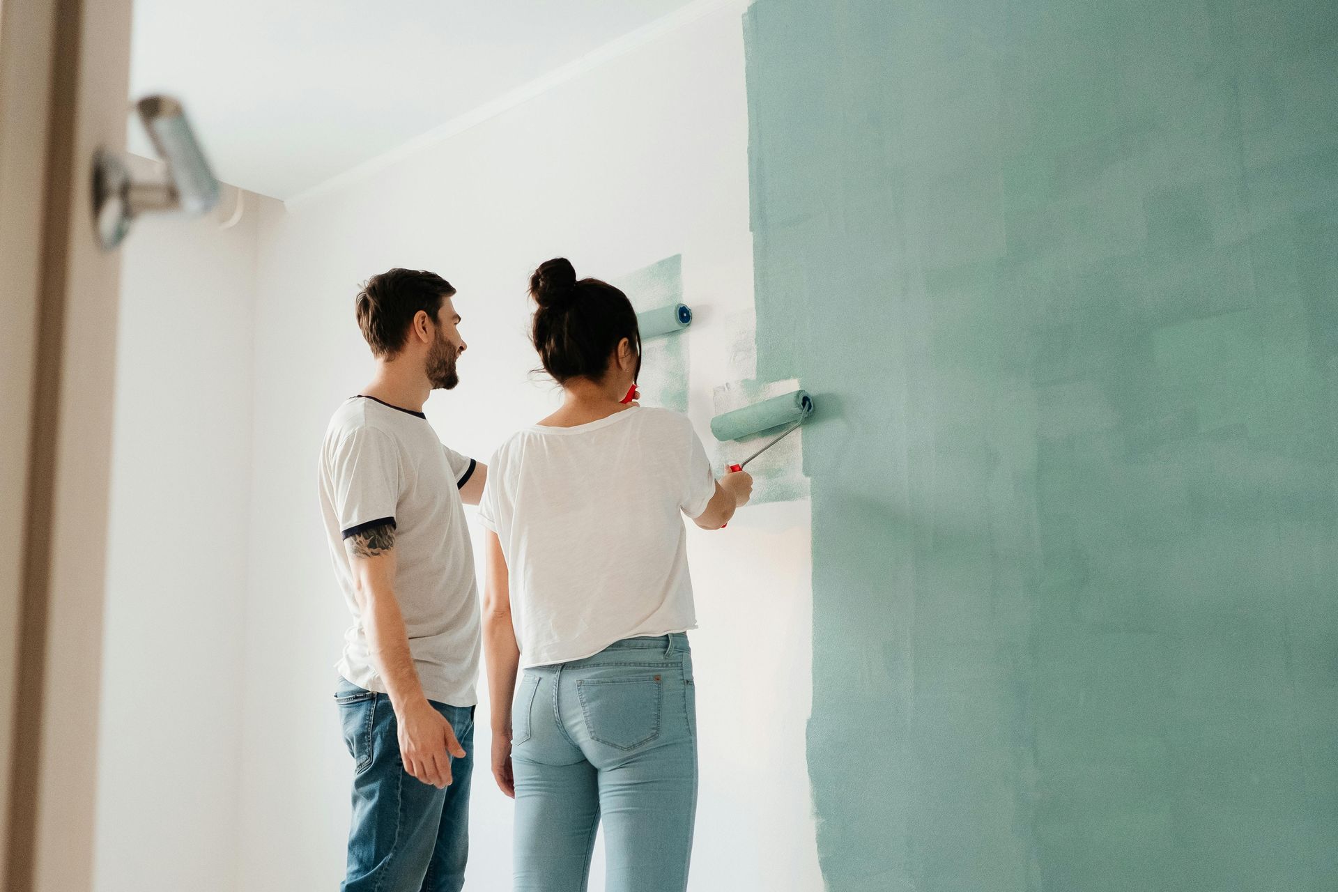 Two people painting a wall white and teal in a bright room