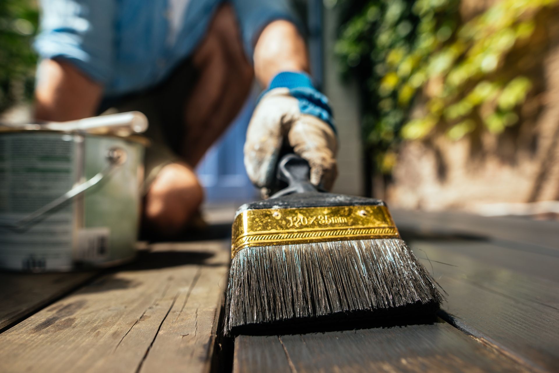 Close-up of a man preparing wooden deck with brush and organic oil for deck finish restoration.