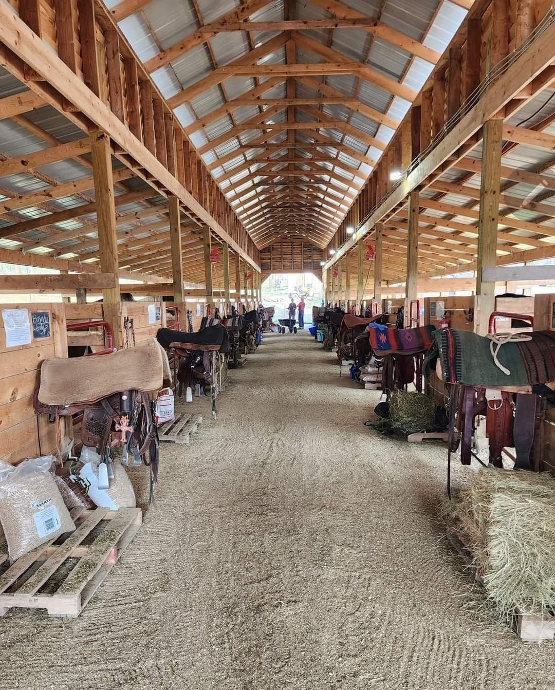 a long hallway in a barn filled with horses and saddlebags .