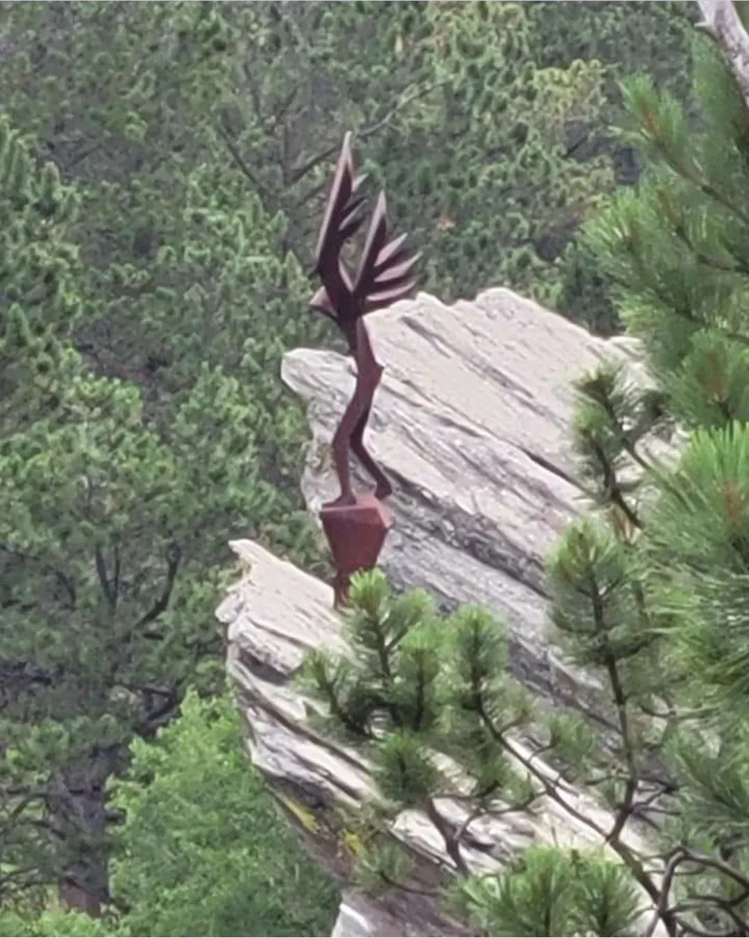a statue of a bird is sitting on top of a rock surrounded by trees .