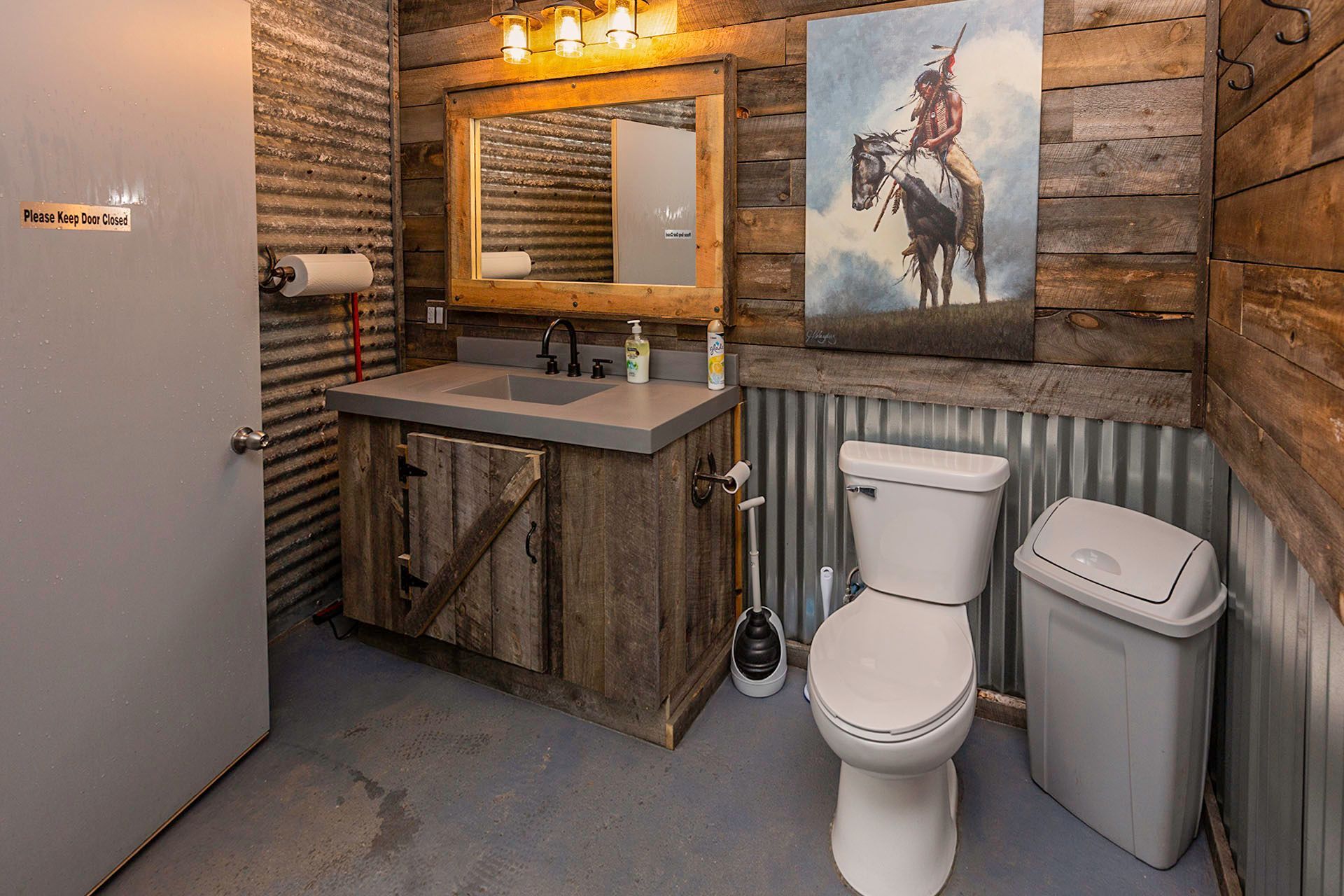 a bathroom with a toilet , sink , mirror and a painting on the wall .