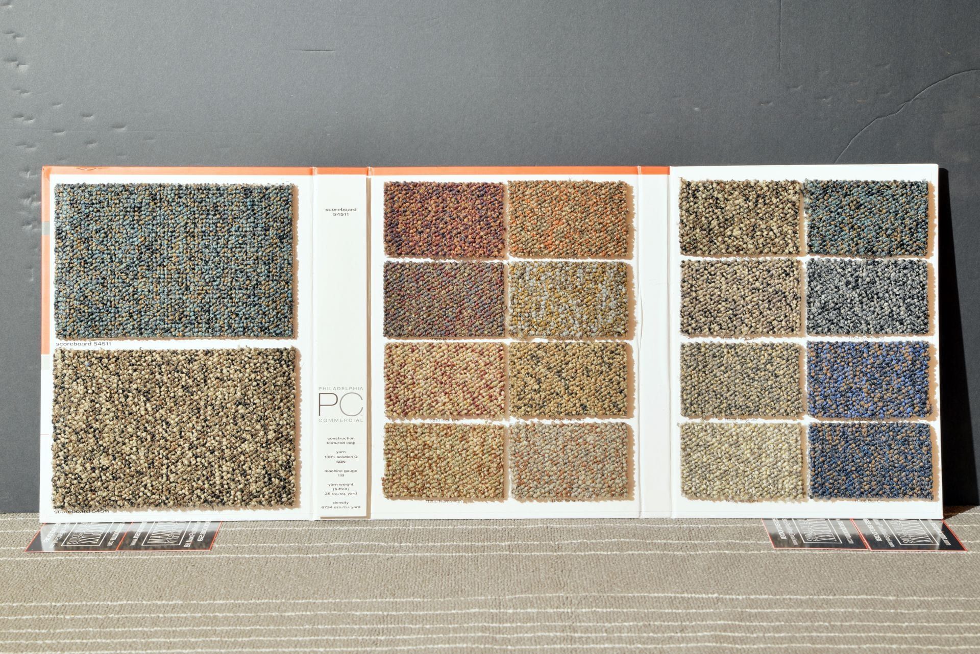 A carpet swatch book is open to a page showing different shades of carpet