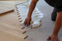 A man is applying glue to a wooden floor with a spatula.