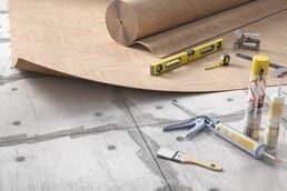 A roll of plywood is sitting on top of a concrete floor next to tools.