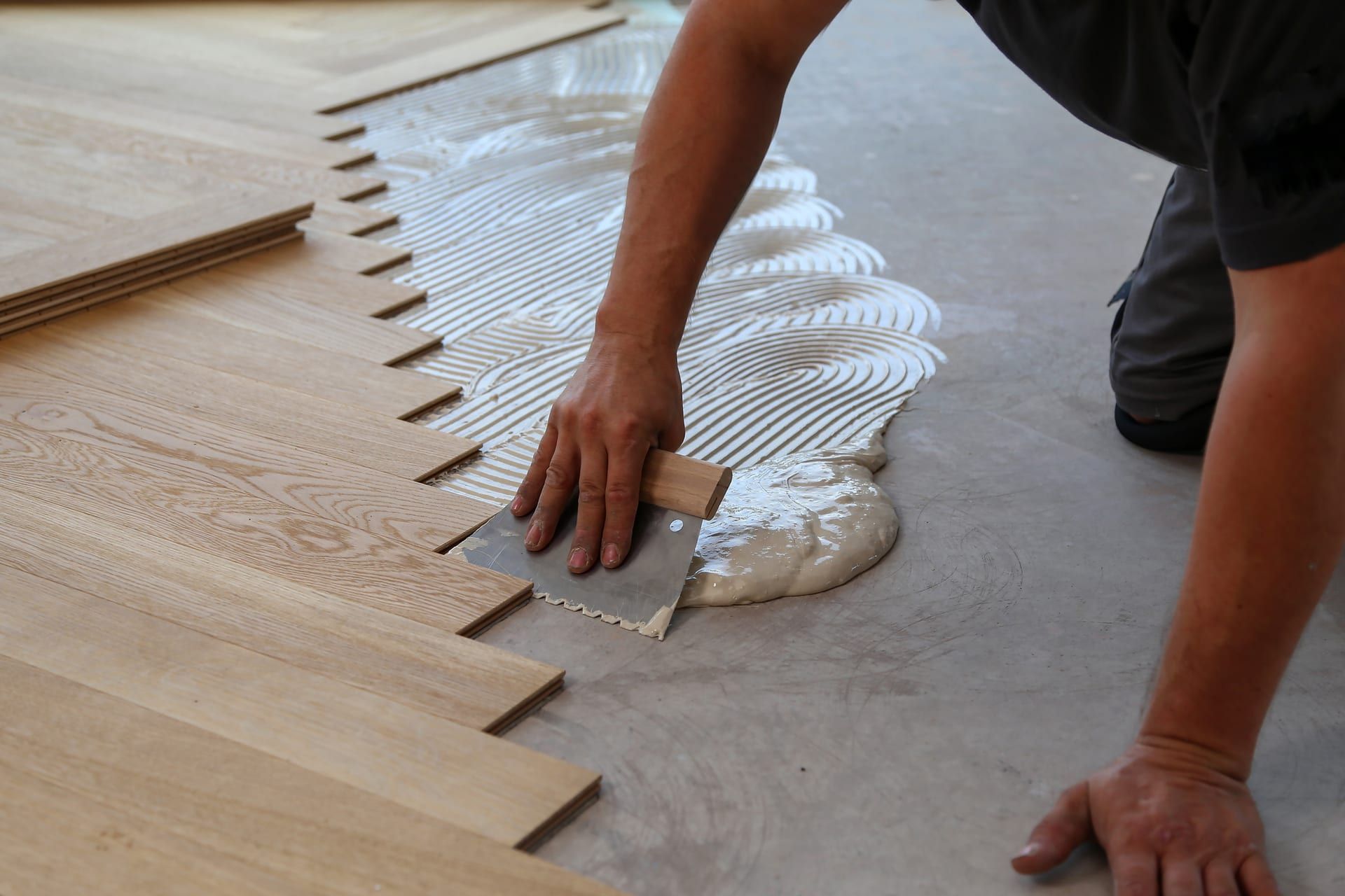 A man is applying glue to a wooden floor with a spatula.