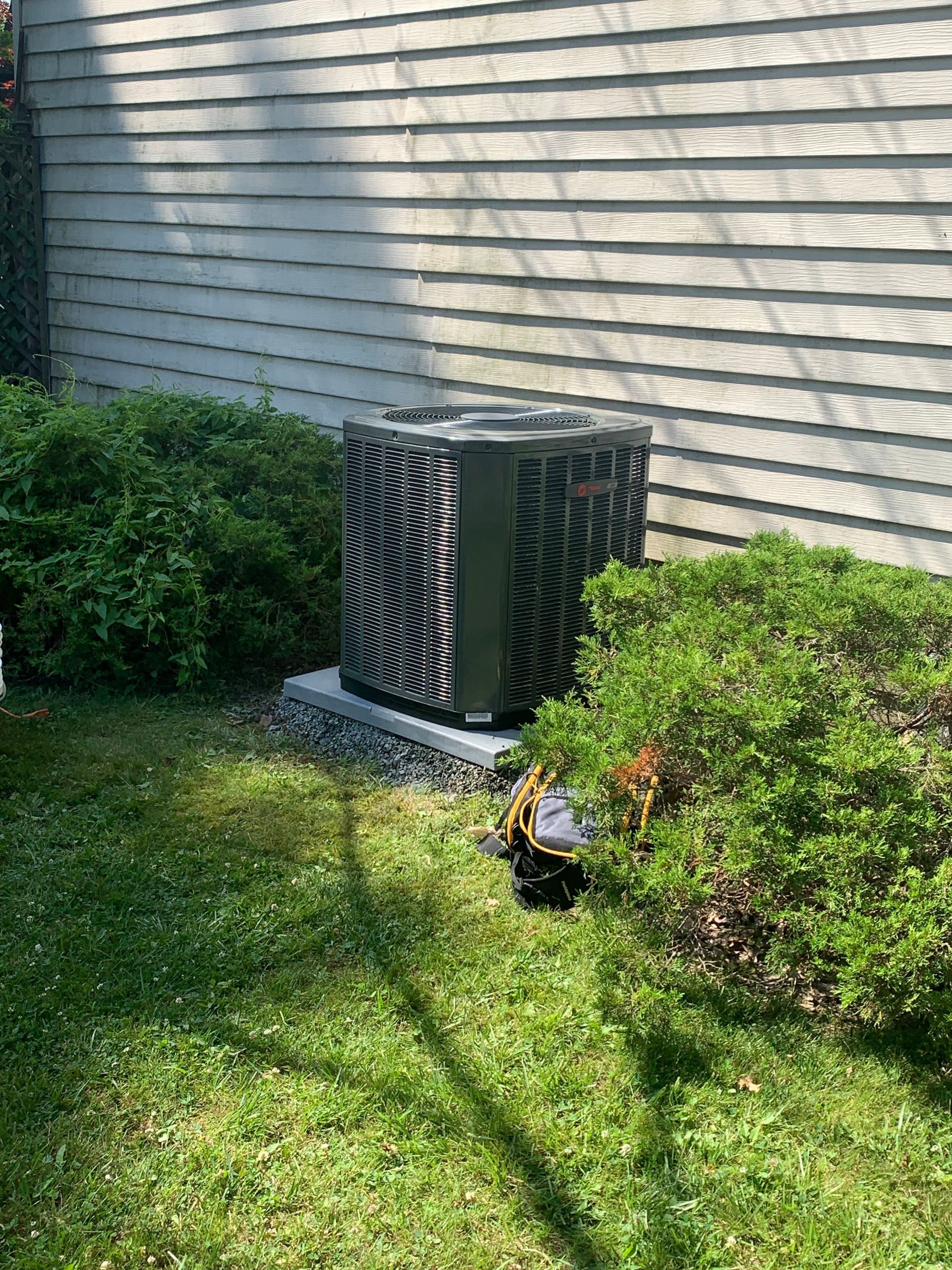 An air conditioner is sitting in the grass in front of a house.