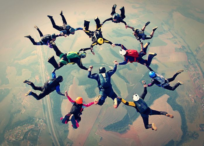 Image of a team of parachuters holding hands in a circle after jumping from an airplane