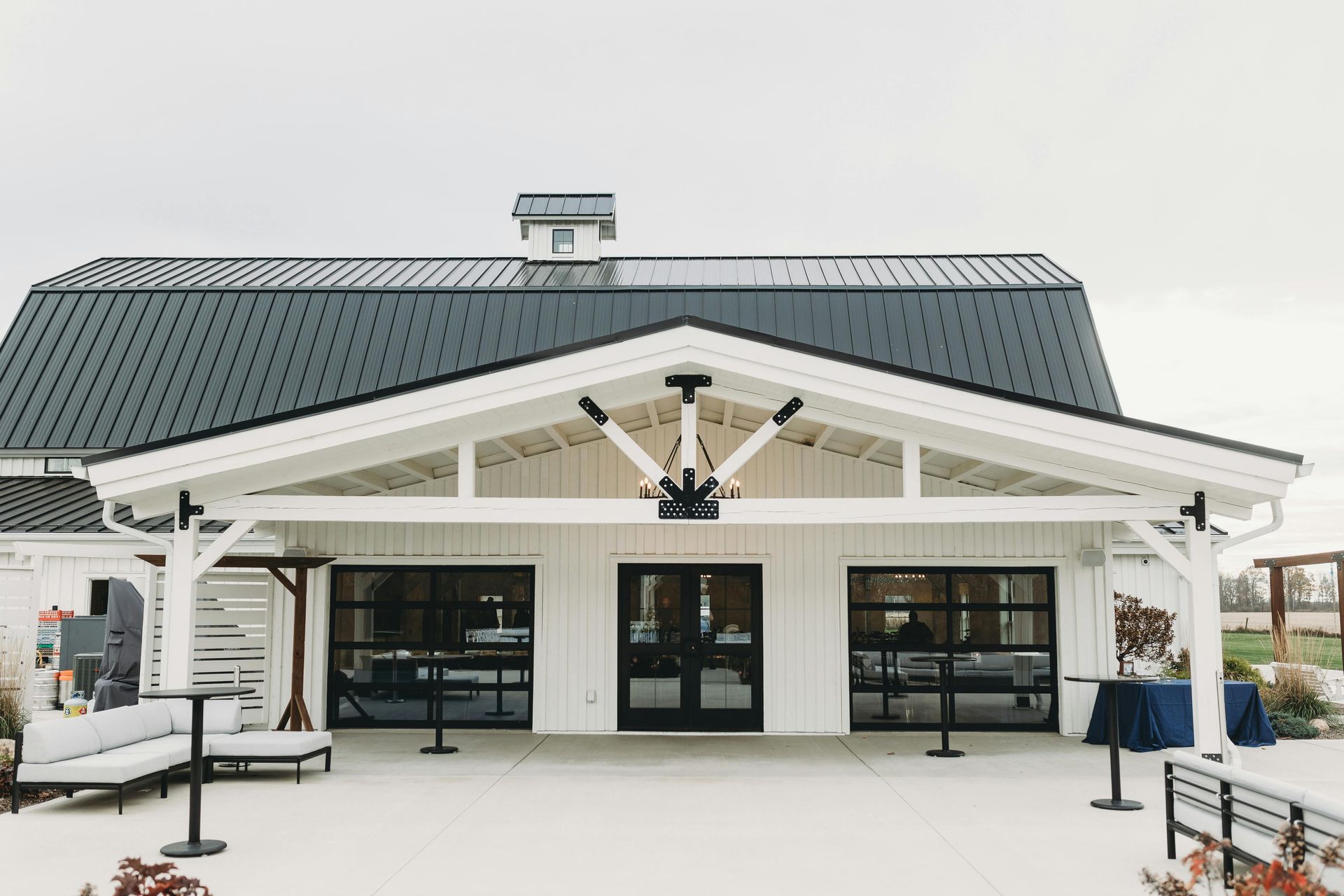White barn-style building with black trim, glass doors, and a dark roof under a cloudy sky.