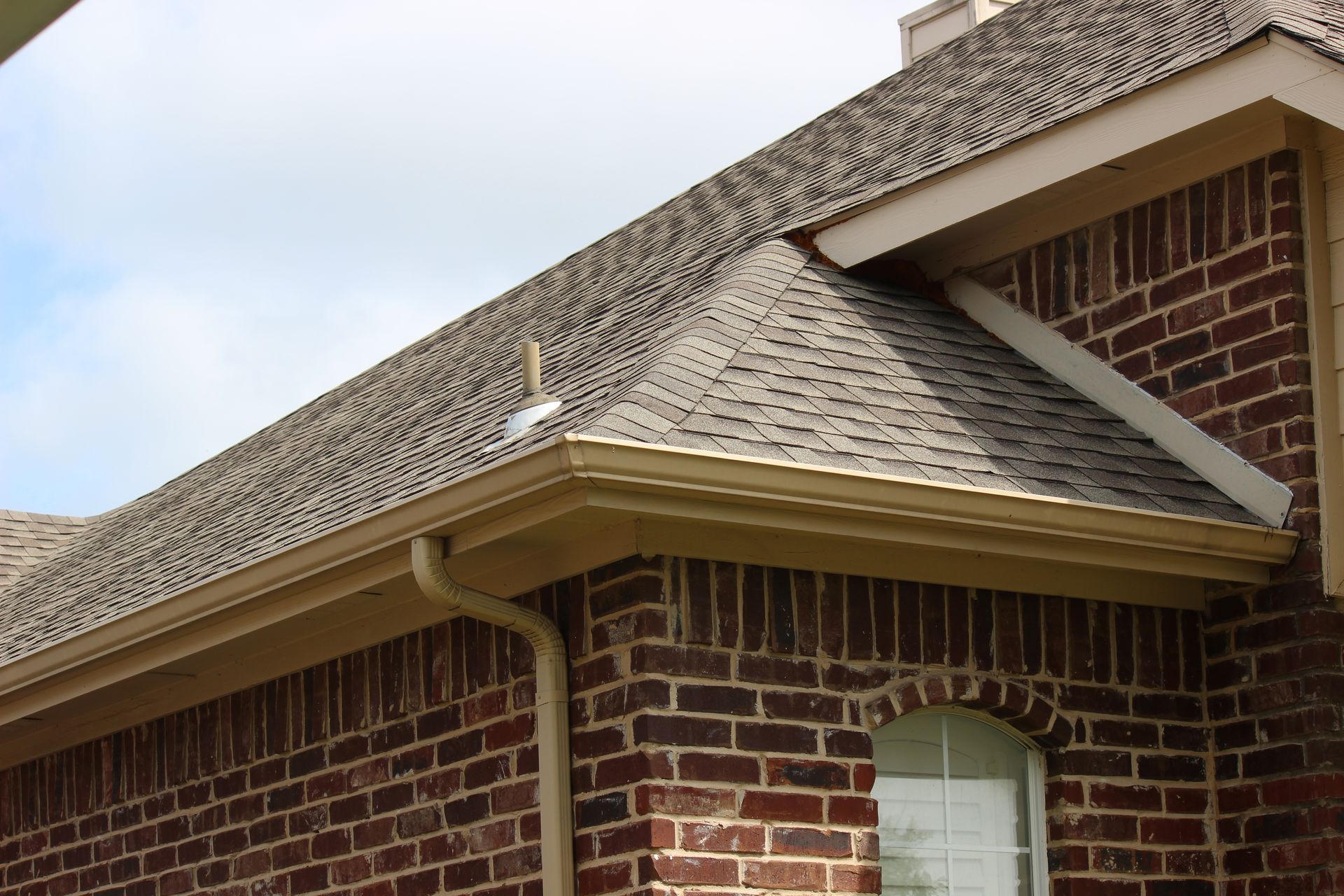 Brick house exterior with roof, gutter, and a window.