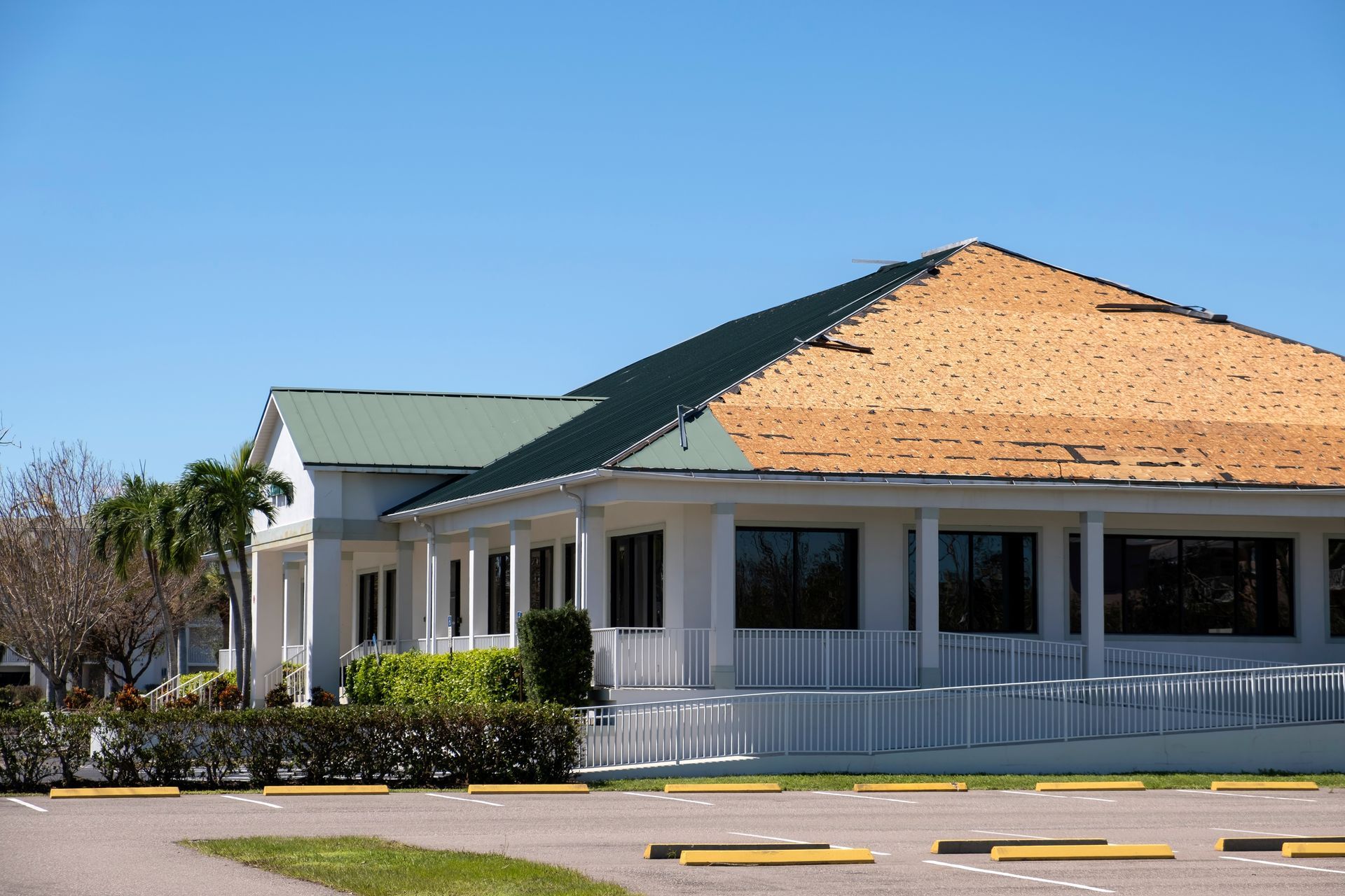 Building with green metal roof, partial roofing removed, parked cars in front.
