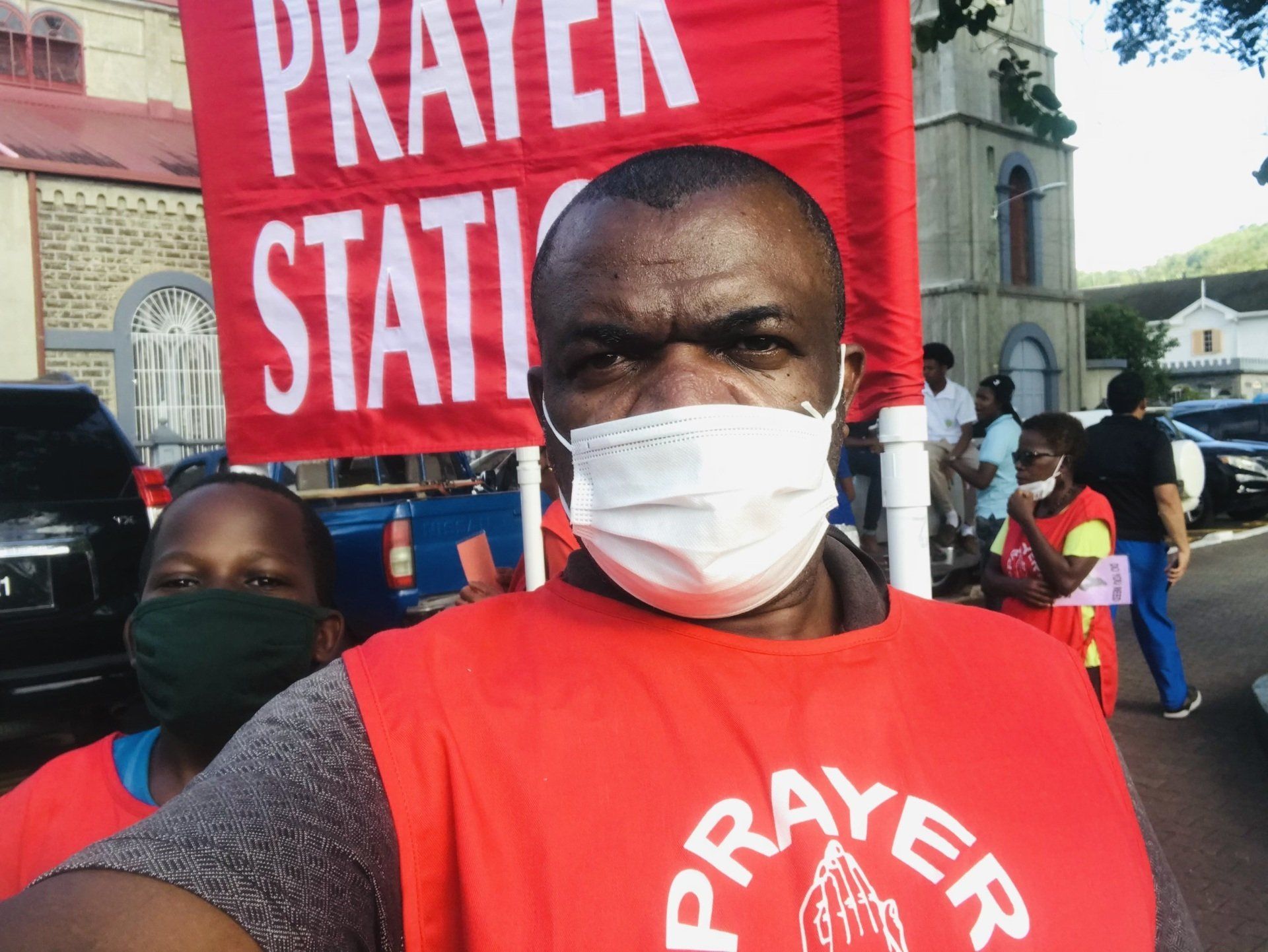 A man wearing a mask is holding a sign that says prayer station