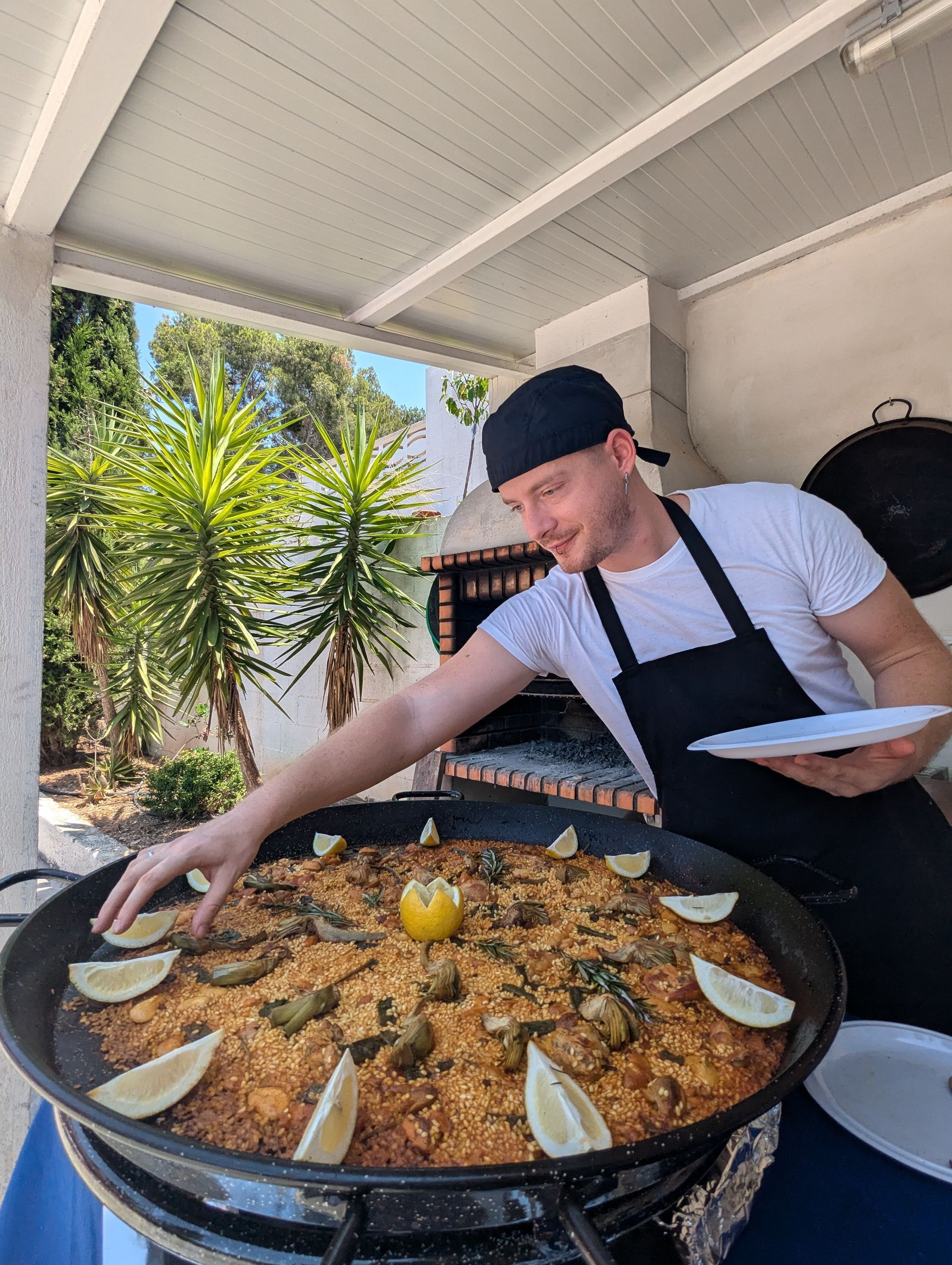 Chef arranging lemon slices on a large paella pan, outdoors.