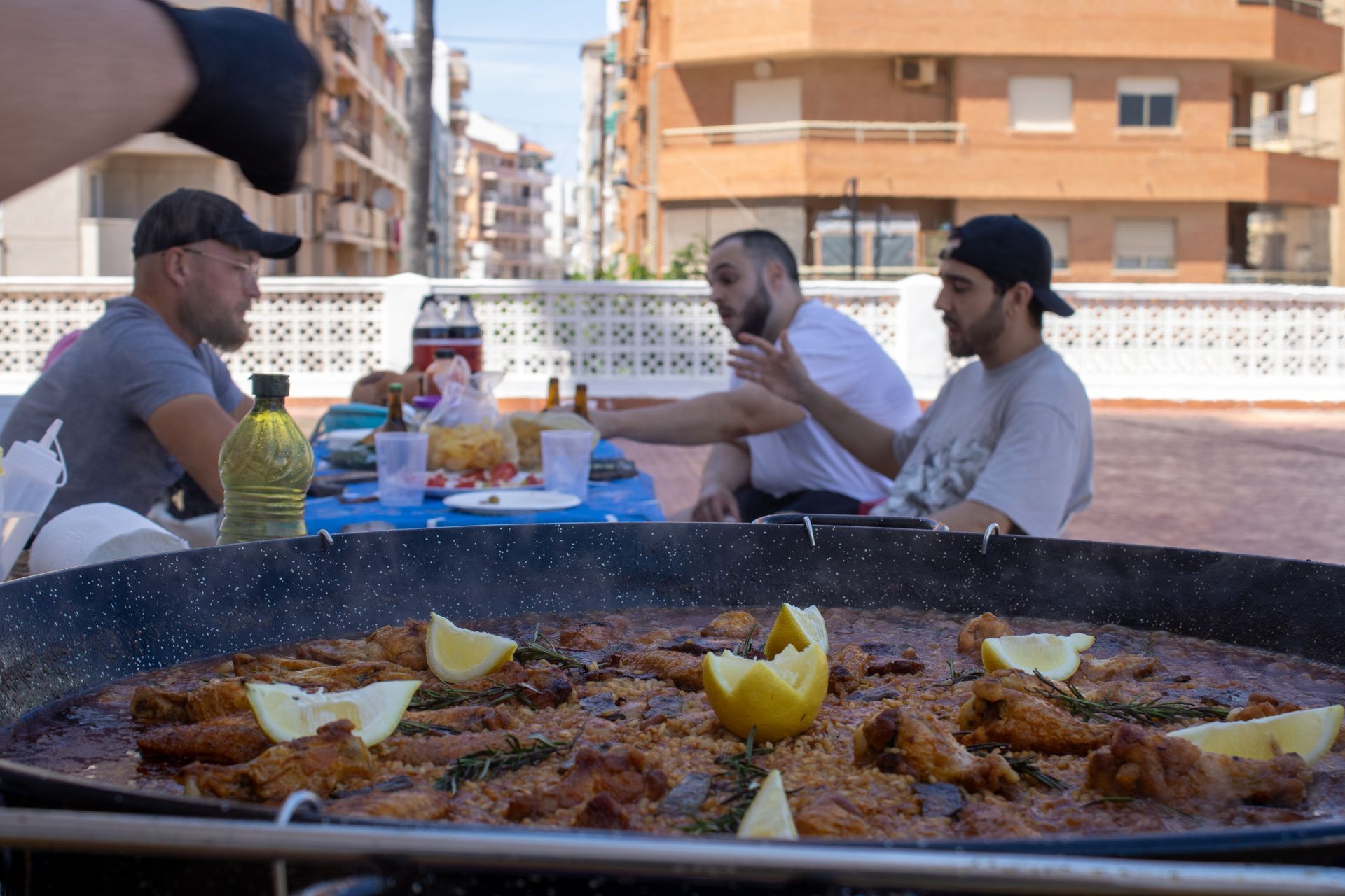 People gathered around a large paella pan on a rooftop, preparing to eat.