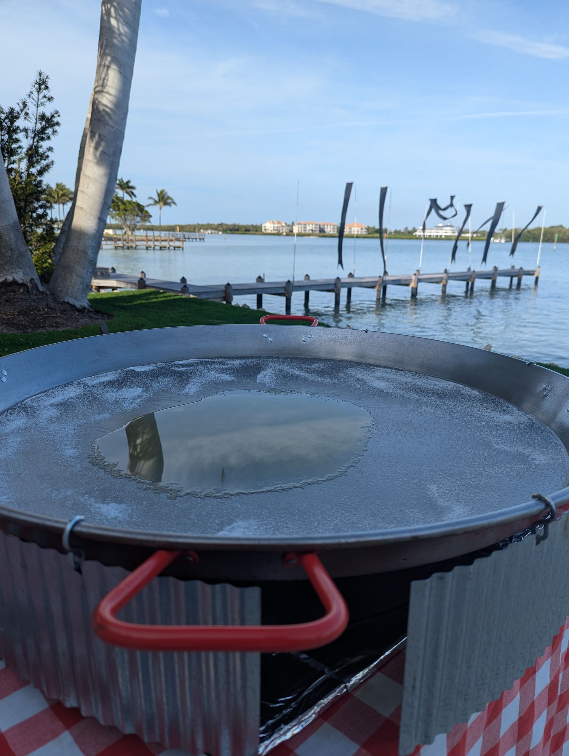 Large paella pan on a stand outdoors, overlooking a dock and water.