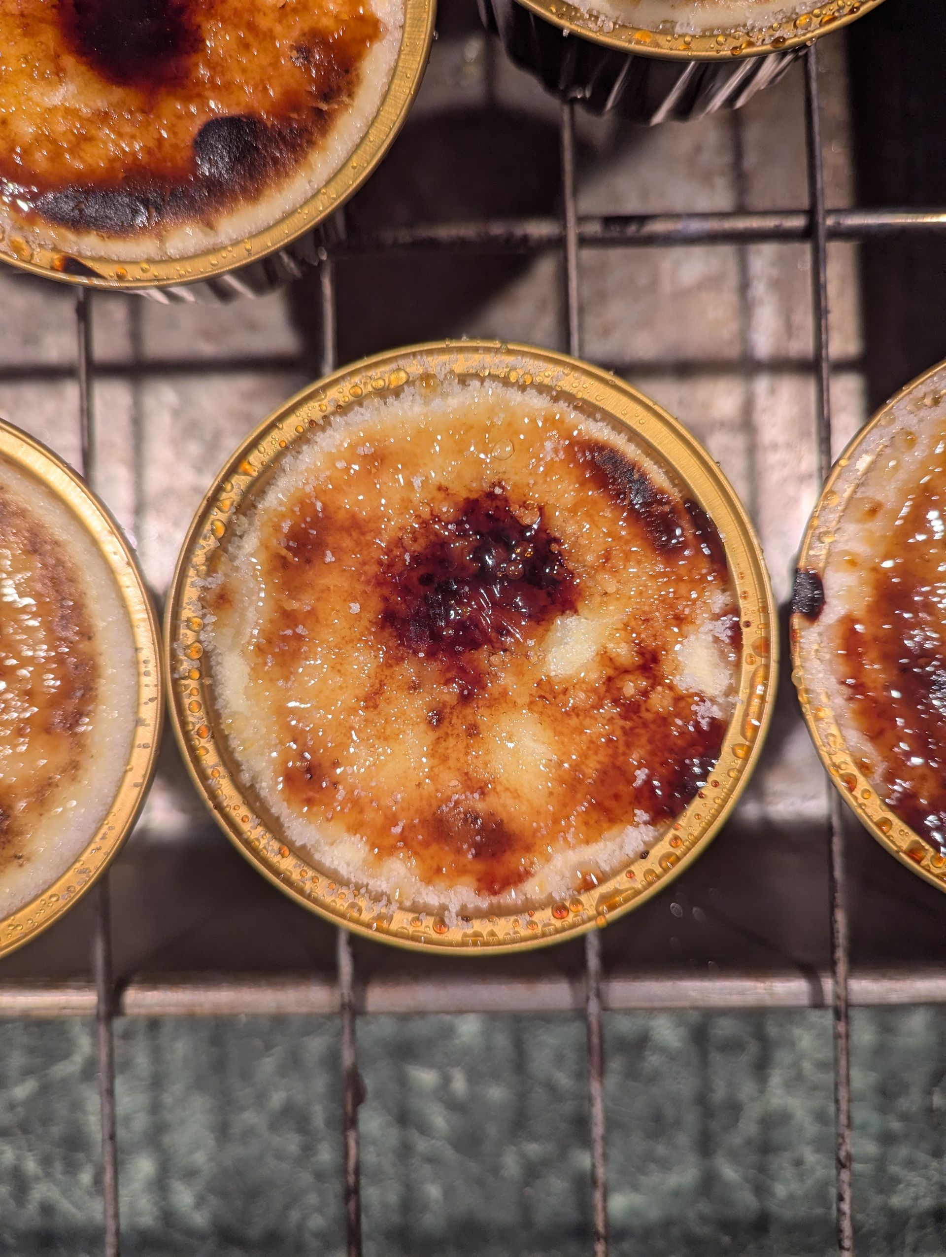 basque cheescake, Crème brûlée desserts in golden ramekins, with a caramelized sugar topping, on a wire rack.