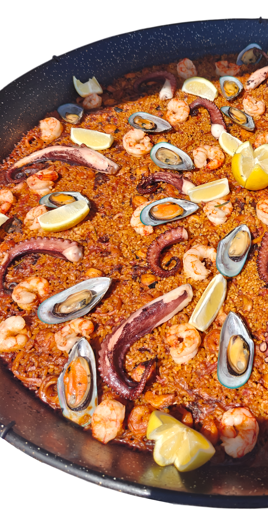 Paella with shrimp, mussels, and lemon wedges in a large, black pan.