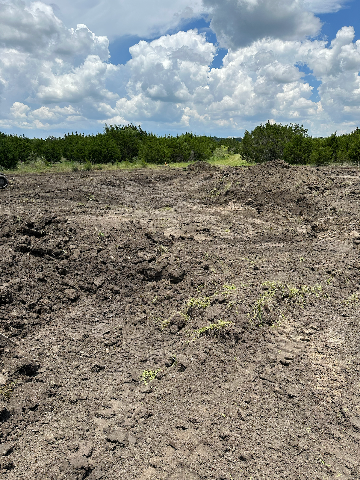 A large pile of dirt in a field with trees in the background