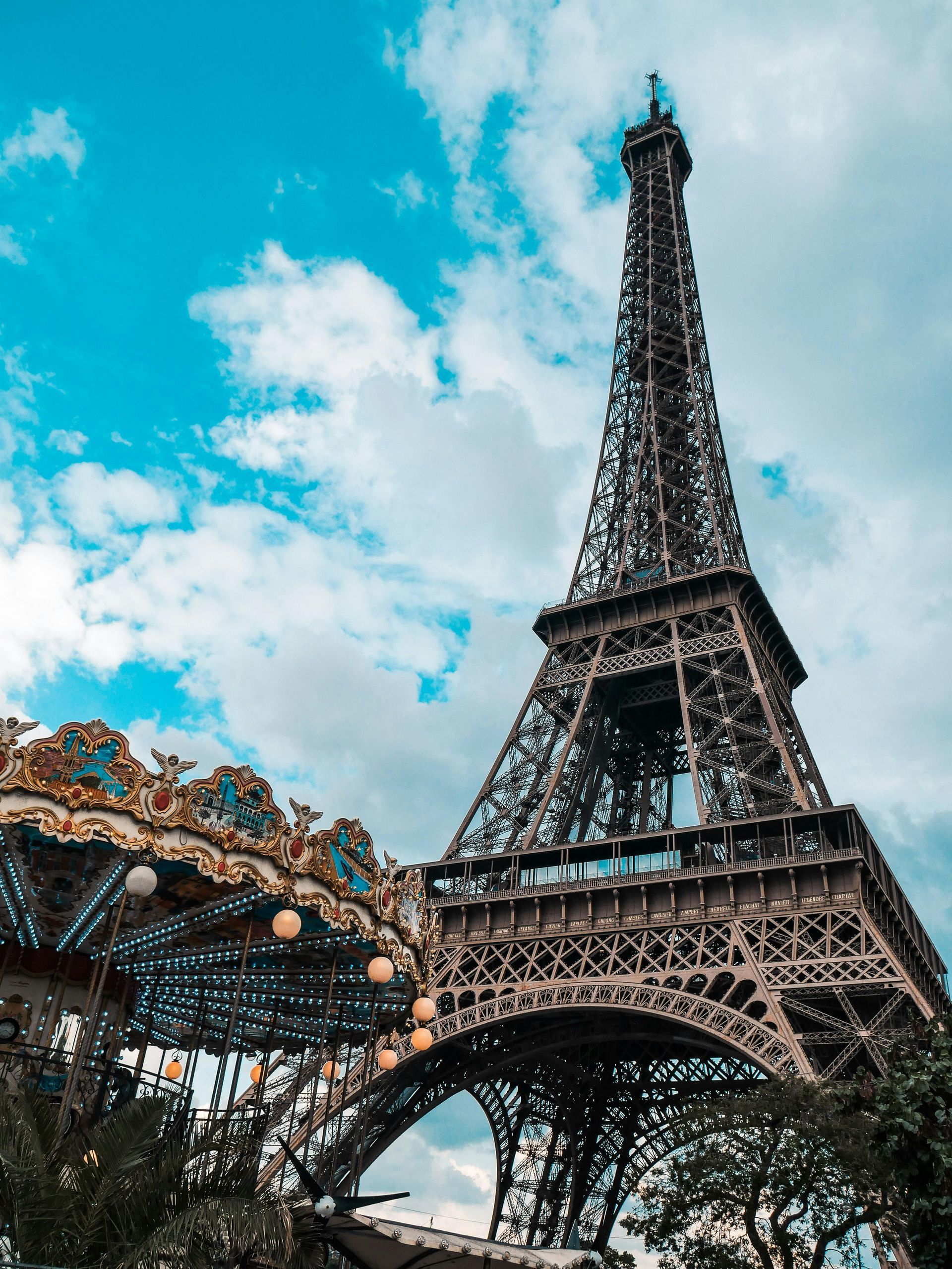 Eiffel Tower in Paris, France, with a carousel in the foreground under a cloudy blue sky.