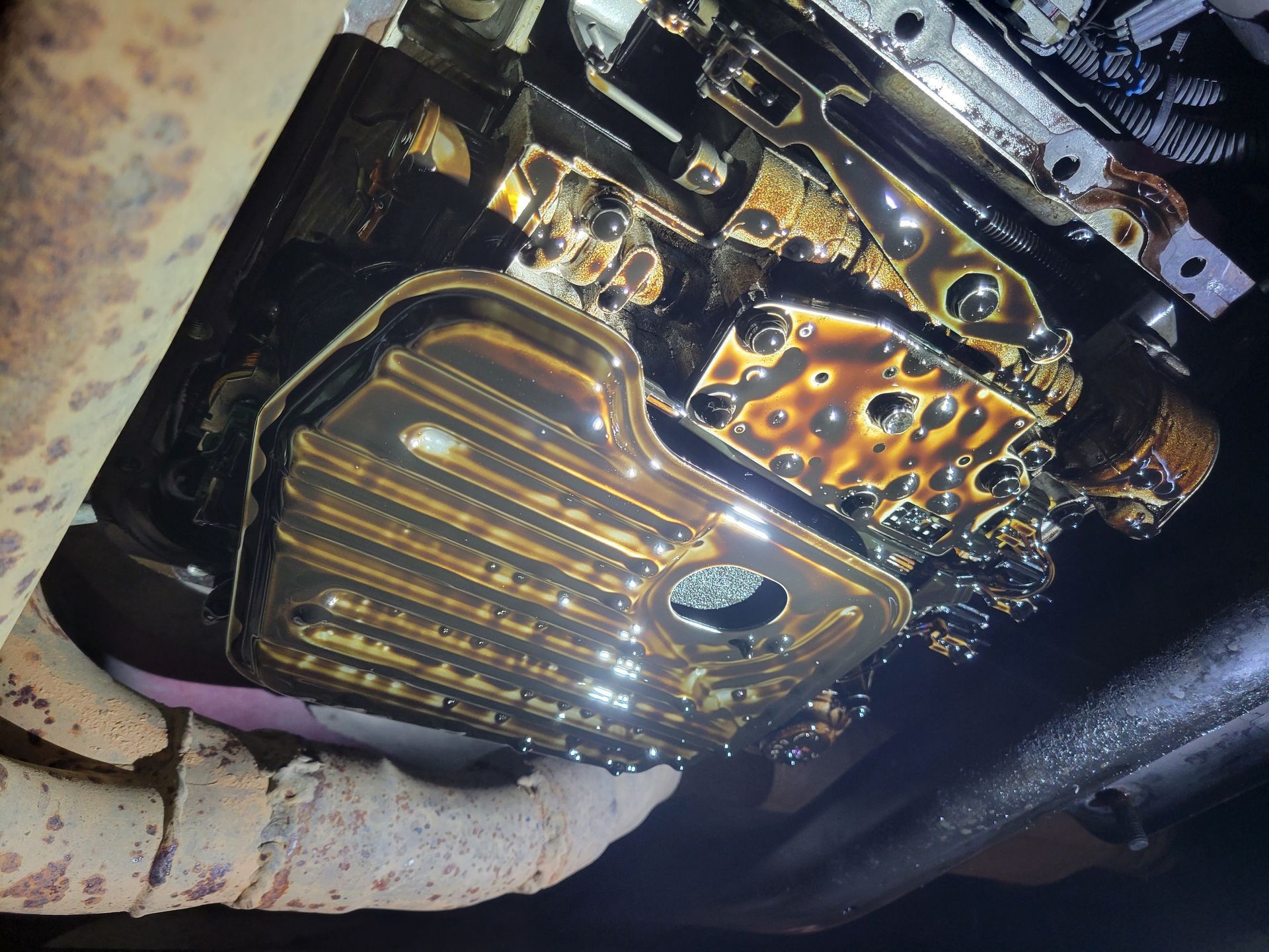 Underside of a car with oil pan and engine components visible, covered in dark oil. | Countryside Automotive