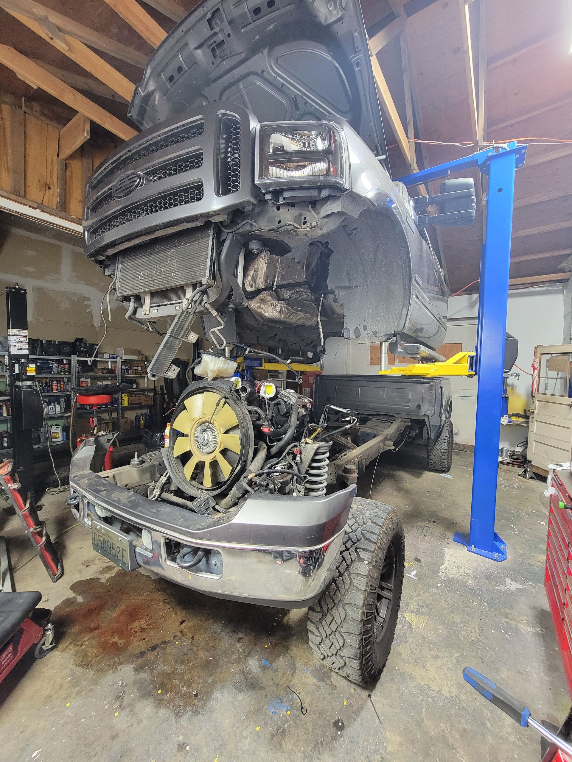 Truck on a lift in a garage, engine exposed. Blue lift arms supporting the vehicle. | Countryside Automotive