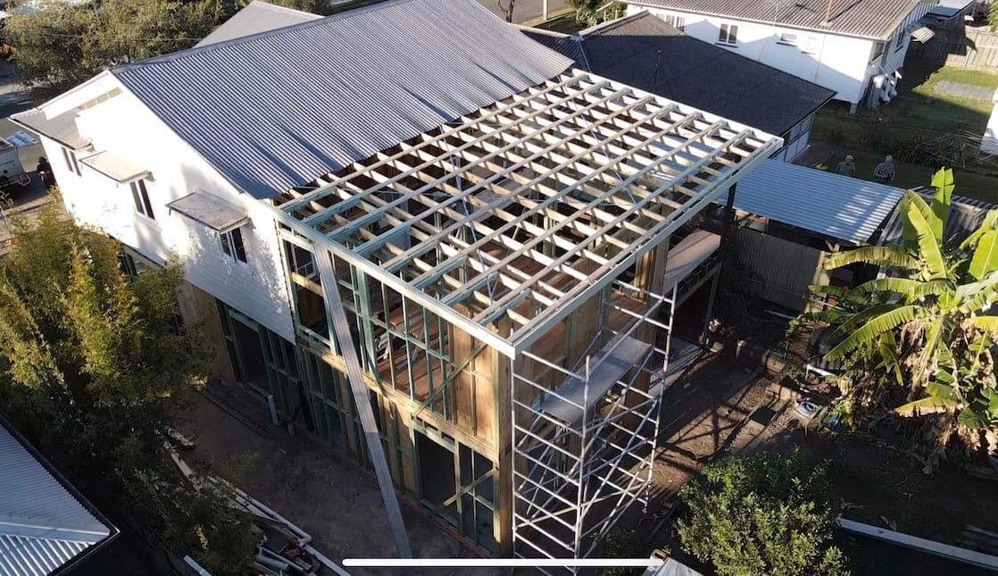House under construction: wooden frame, scaffolding, partial roof, white siding.