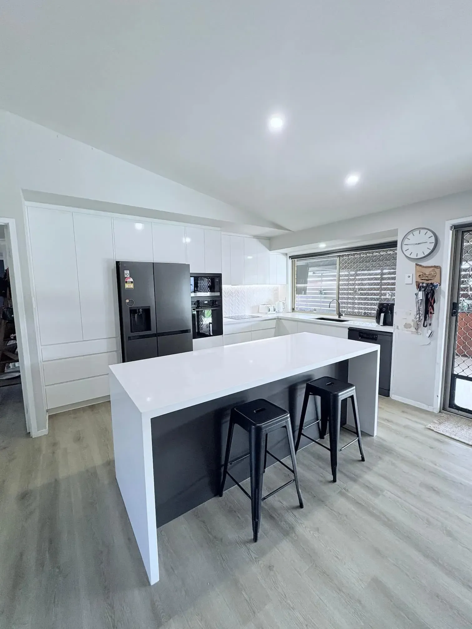 Modern kitchen with white cabinets, dark island with stools, and black refrigerator.
